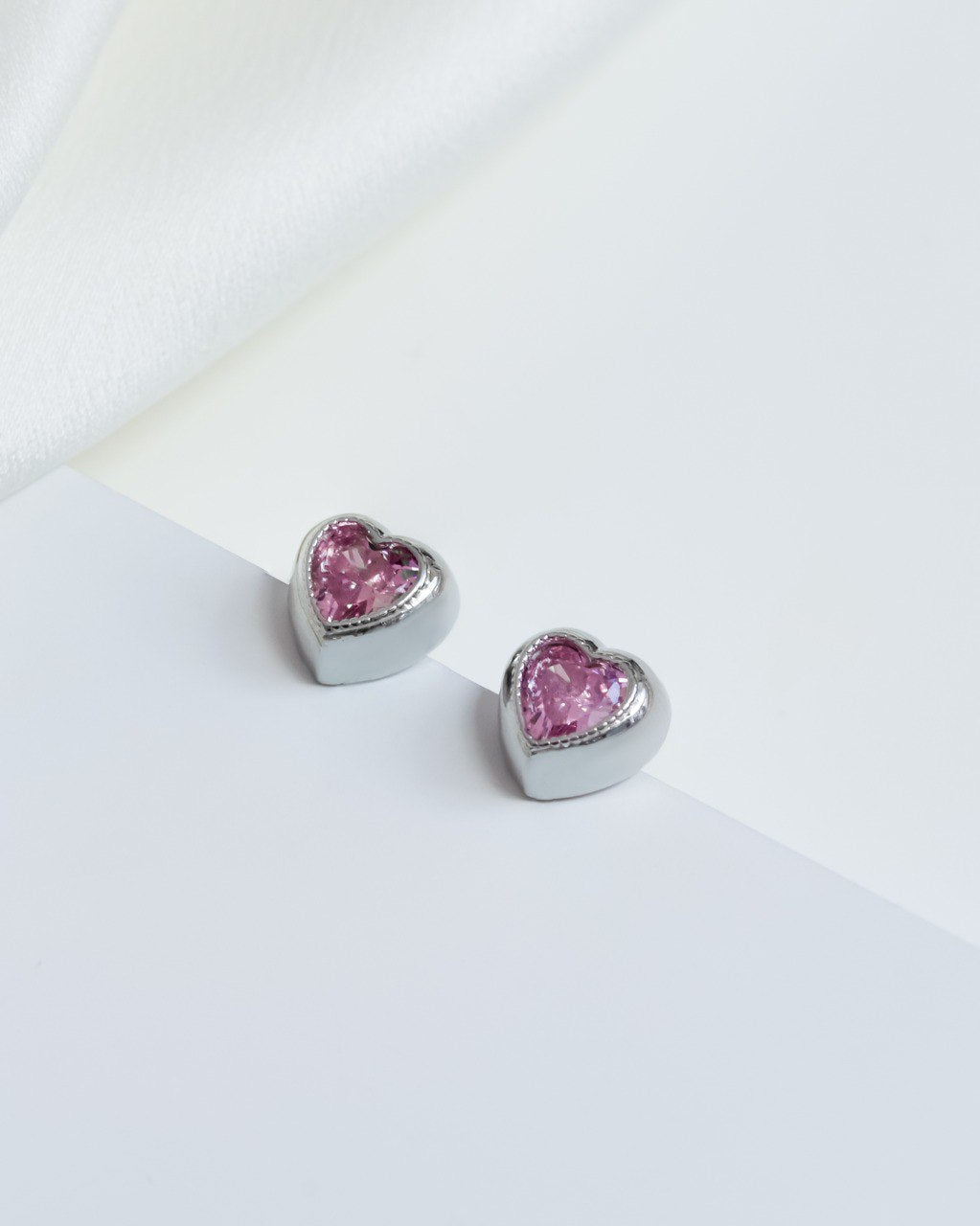 Close-up of heart-shaped earrings adorned with pink zirconias in a rhodium-plated setting, highlighting their sparkling and stylish design.